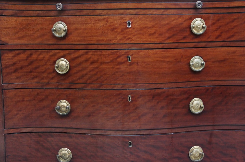An 18th-century Georgian mahogany chest of drawers with a serpentine front, four graduated drawers, circular brass ring handles, a pull-out brushing slide, and bracket feet. View X