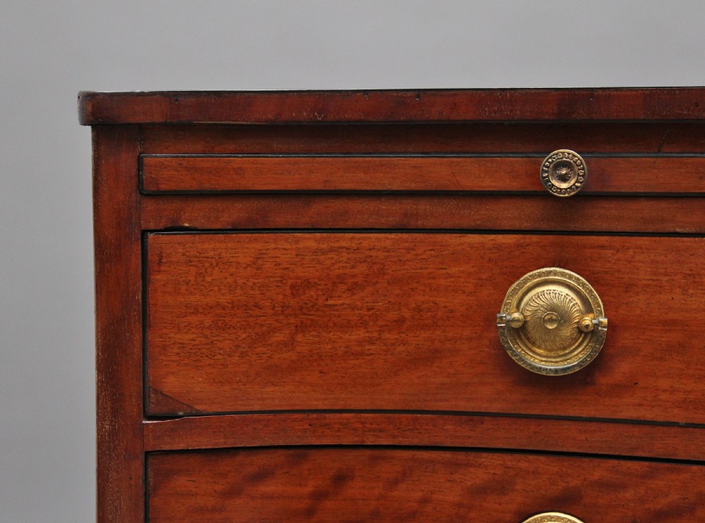 An 18th-century Georgian mahogany chest of drawers with a serpentine front, four graduated drawers, circular brass ring handles, a pull-out brushing slide, and bracket feet. View XI