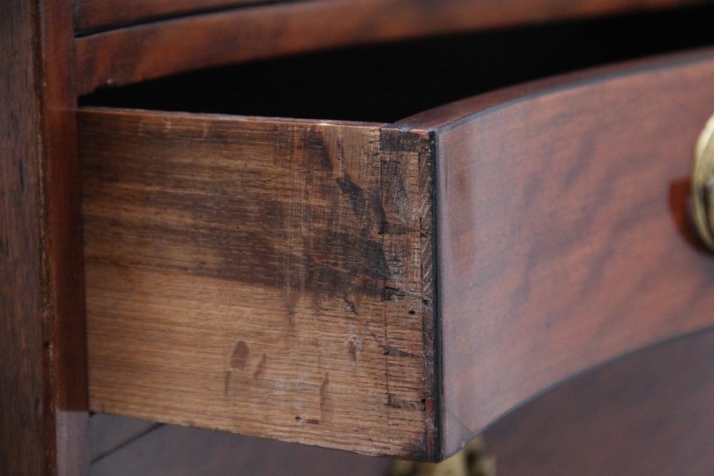 An 18th-century Georgian mahogany chest of drawers with a serpentine front, four graduated drawers, circular brass ring handles, a pull-out brushing slide, and bracket feet. View XII