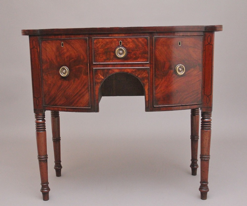 An early 19th-century bowfront mahogany sideboard with turned legs, brass ring drop handles, and central arch drawer.