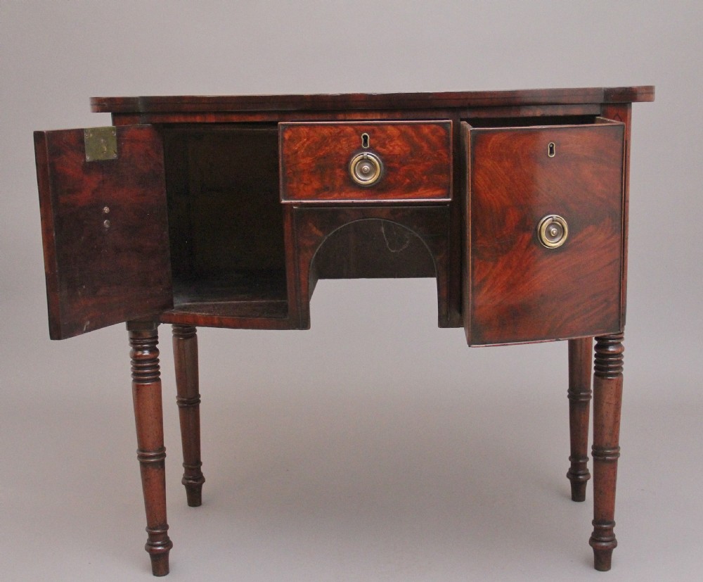 An early 19th-century bowfront mahogany sideboard with turned legs, brass ring drop handles, and central arch drawer. View II