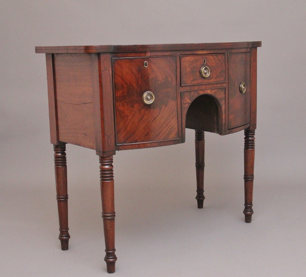 An early 19th-century bowfront mahogany sideboard with turned legs, brass ring drop handles, and central arch drawer. View VI