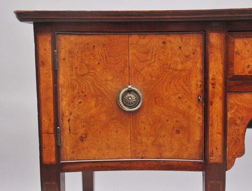 A nineteenth-century mahogany sideboard featuring burr elm veneer panels, two side cupboards, a central drawer above an arched apron, and four tapered square legs with brass ring handles. View III