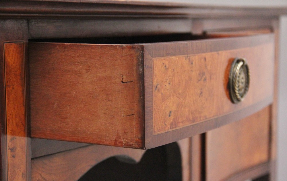 A nineteenth-century mahogany sideboard featuring burr elm veneer panels, two side cupboards, a central drawer above an arched apron, and four tapered square legs with brass ring handles. View VIII