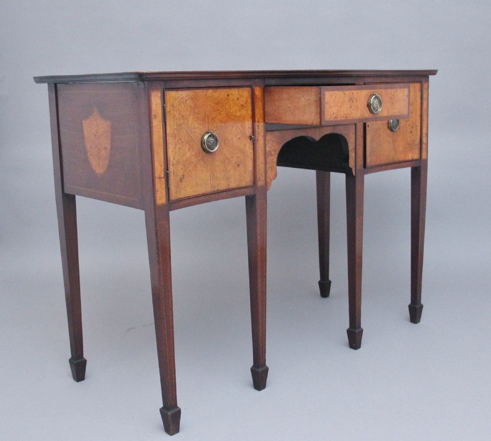 A nineteenth-century mahogany sideboard featuring burr elm veneer panels, two side cupboards, a central drawer above an arched apron, and four tapered square legs with brass ring handles. View X