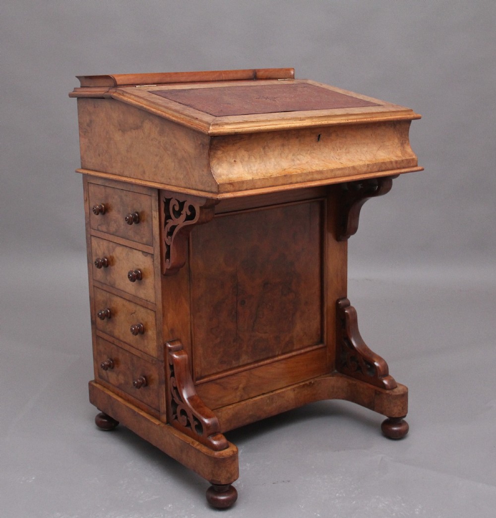 A 19th-century burr walnut Davenport desk featuring a sloped leather writing surface, side drawers with turned knobs, and carved decorative brackets.
