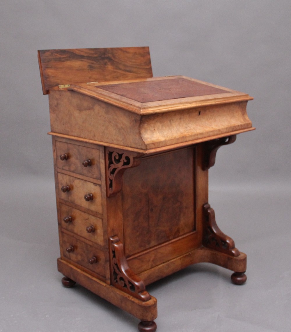 A 19th-century burr walnut Davenport desk featuring a sloped leather writing surface, side drawers with turned knobs, and carved decorative brackets. View IV