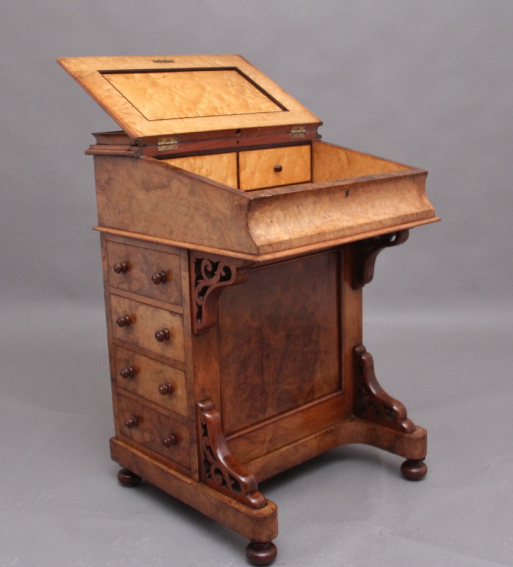 A 19th-century burr walnut Davenport desk featuring a sloped leather writing surface, side drawers with turned knobs, and carved decorative brackets. View V
