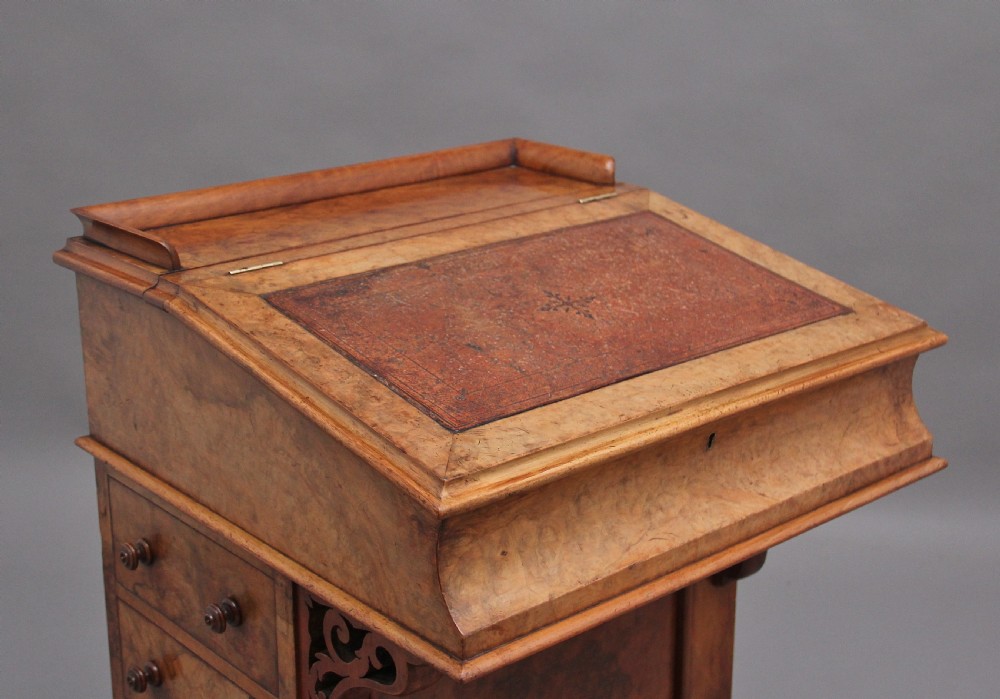 A 19th-century burr walnut Davenport desk featuring a sloped leather writing surface, side drawers with turned knobs, and carved decorative brackets. View VI