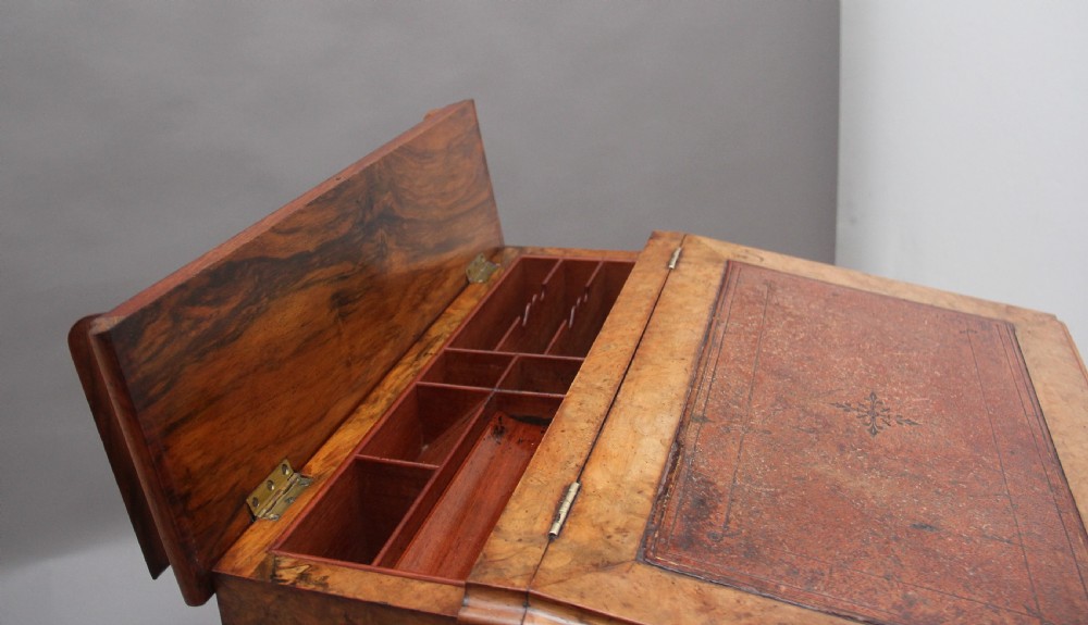 A 19th-century burr walnut Davenport desk featuring a sloped leather writing surface, side drawers with turned knobs, and carved decorative brackets. View IX