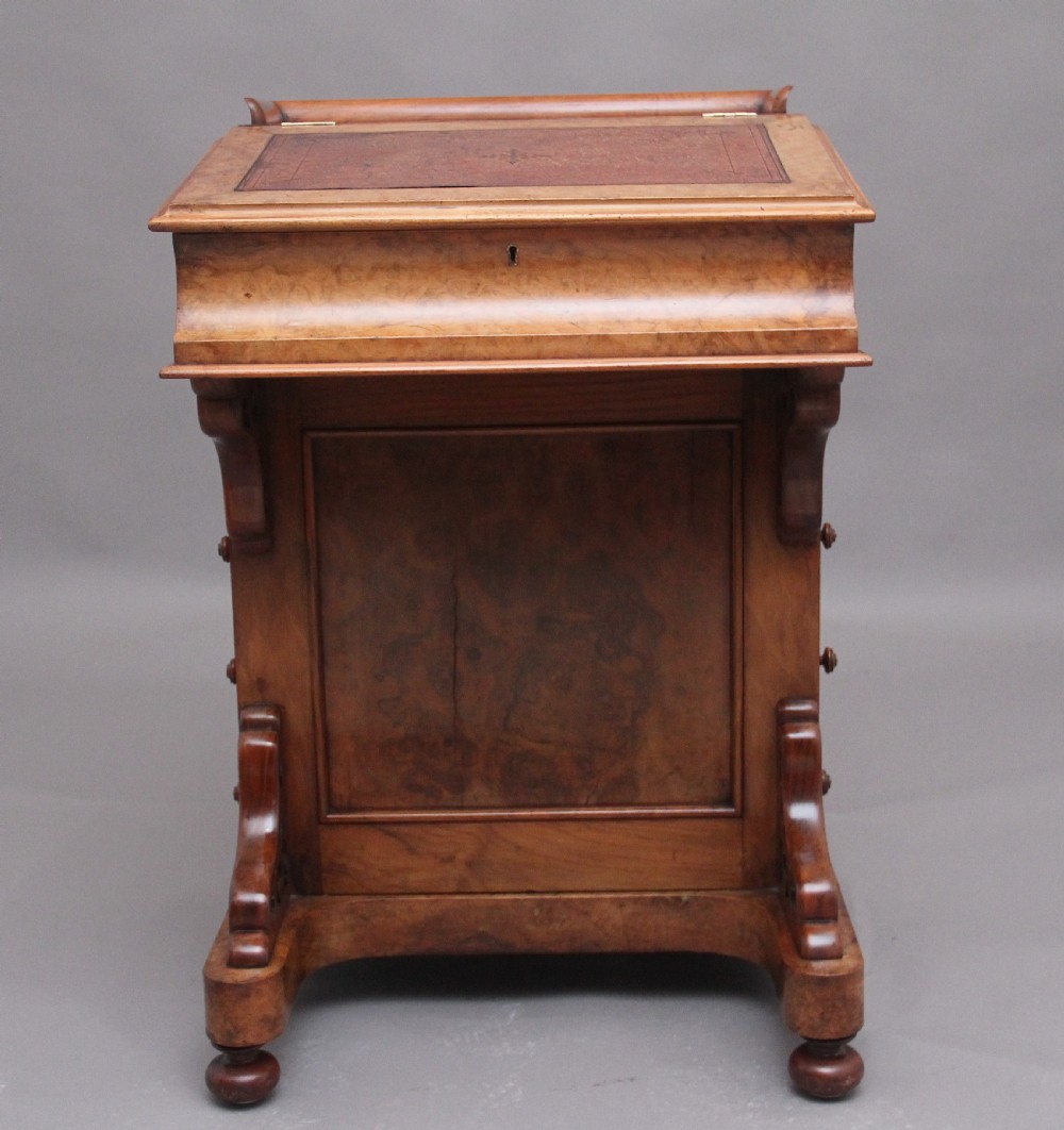 A 19th-century burr walnut Davenport desk featuring a sloped leather writing surface, side drawers with turned knobs, and carved decorative brackets. View X