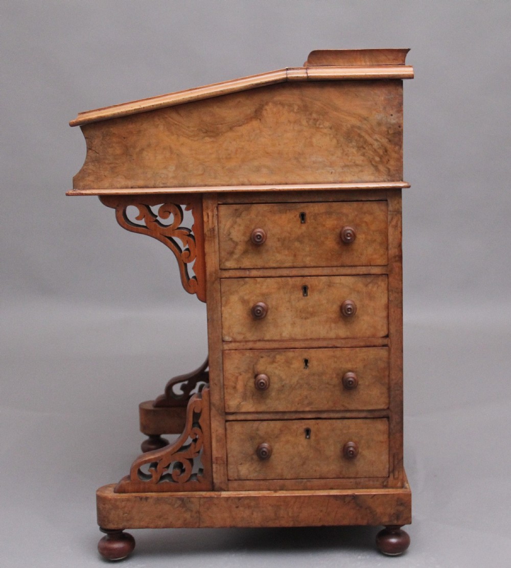 A 19th-century burr walnut Davenport desk featuring a sloped leather writing surface, side drawers with turned knobs, and carved decorative brackets. View XI