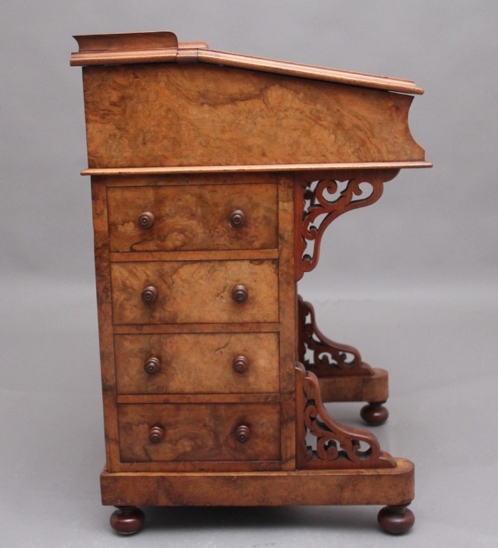 A 19th-century burr walnut Davenport desk featuring a sloped leather writing surface, side drawers with turned knobs, and carved decorative brackets. View XIV