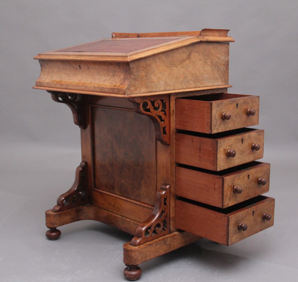 A 19th-century burr walnut Davenport desk featuring a sloped leather writing surface, side drawers with turned knobs, and carved decorative brackets. View XV
