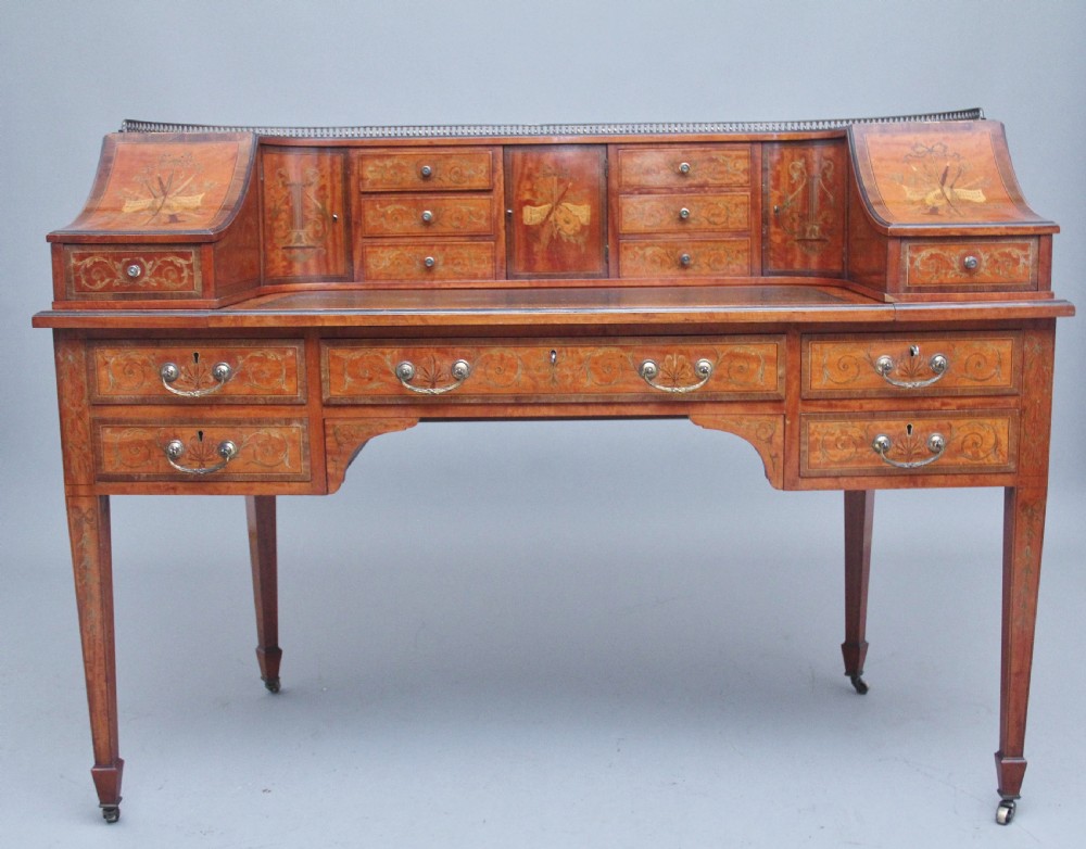 A 19th-century satinwood Carlton House writing desk featuring decorative marquetry, small drawers on a U-shaped superstructure, and tapered square legs with brass castors.