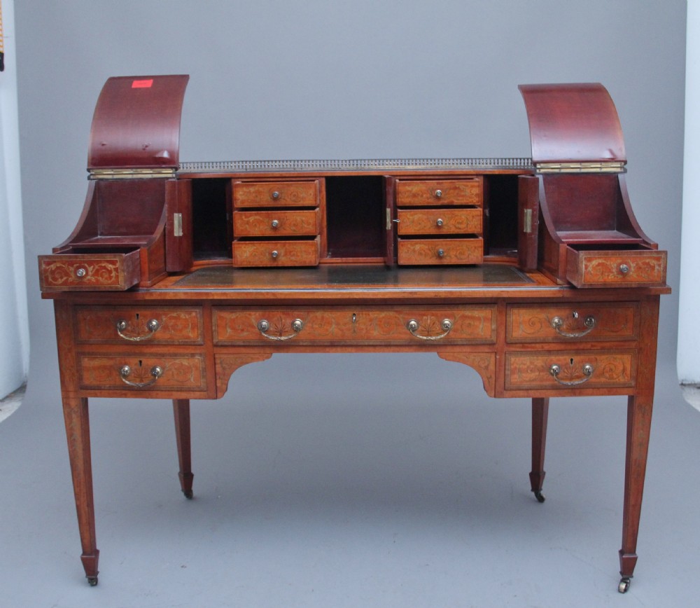 A 19th-century satinwood Carlton House writing desk featuring decorative marquetry, small drawers on a U-shaped superstructure, and tapered square legs with brass castors. View II