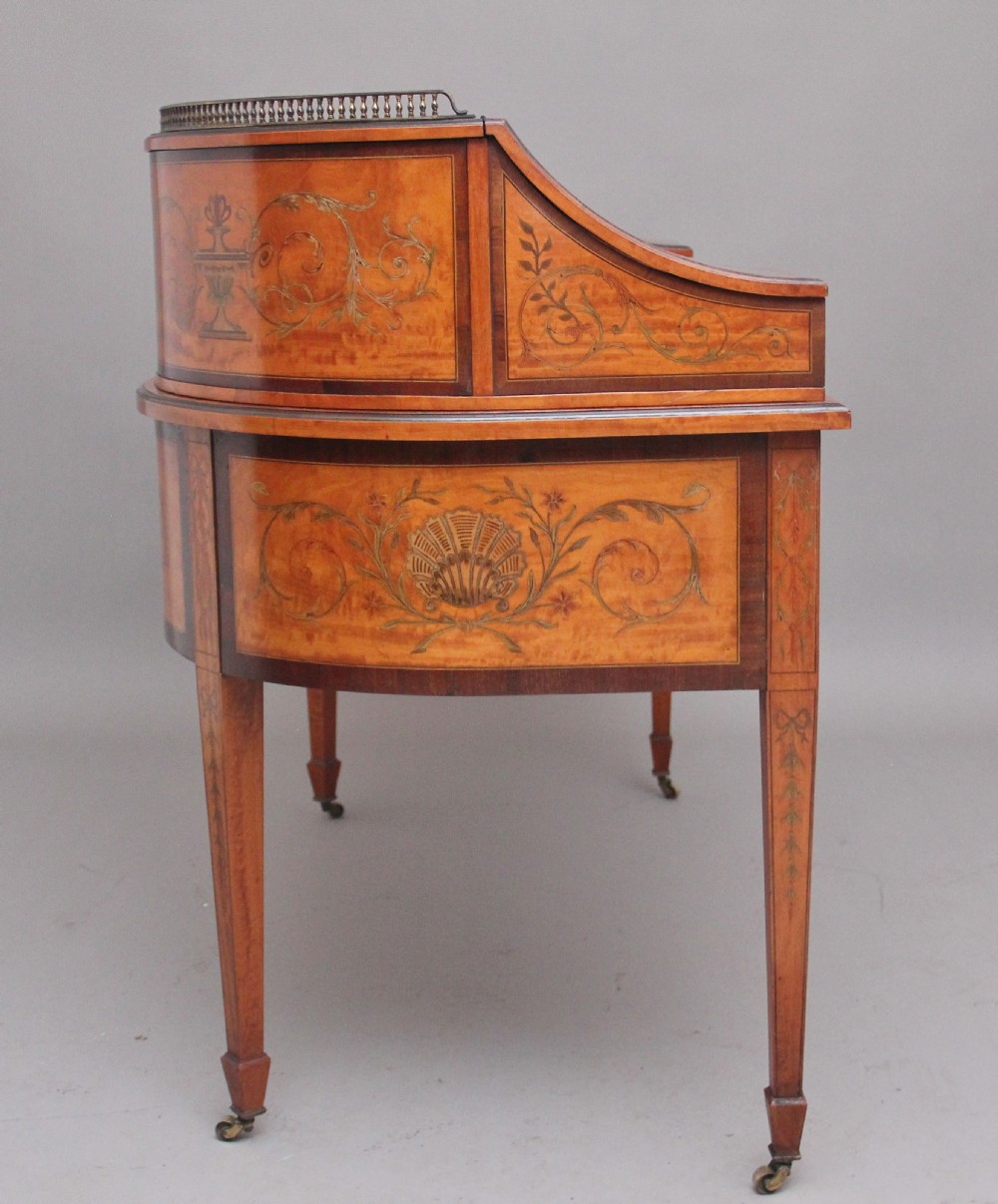 A 19th-century satinwood Carlton House writing desk featuring decorative marquetry, small drawers on a U-shaped superstructure, and tapered square legs with brass castors. View V