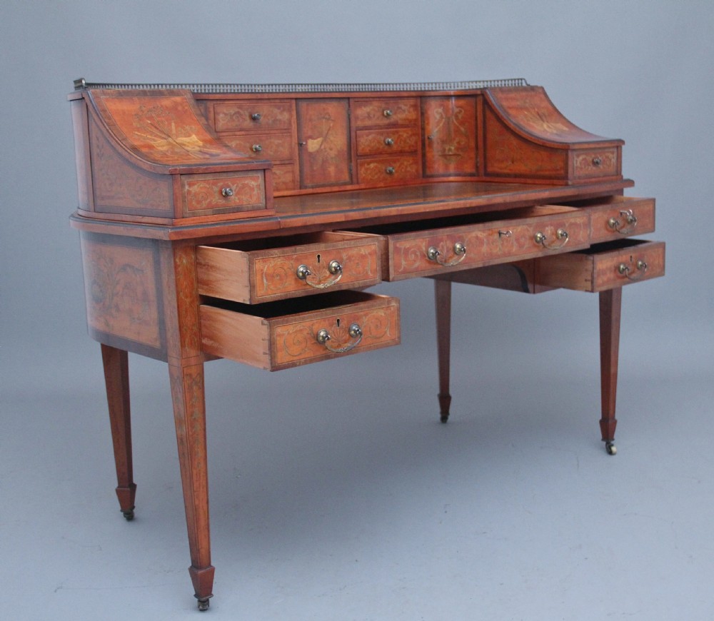 A 19th-century satinwood Carlton House writing desk featuring decorative marquetry, small drawers on a U-shaped superstructure, and tapered square legs with brass castors. View VI