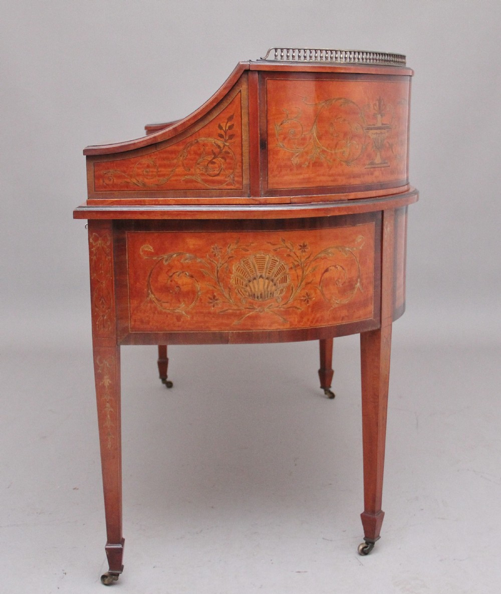 A 19th-century satinwood Carlton House writing desk featuring decorative marquetry, small drawers on a U-shaped superstructure, and tapered square legs with brass castors. View XI