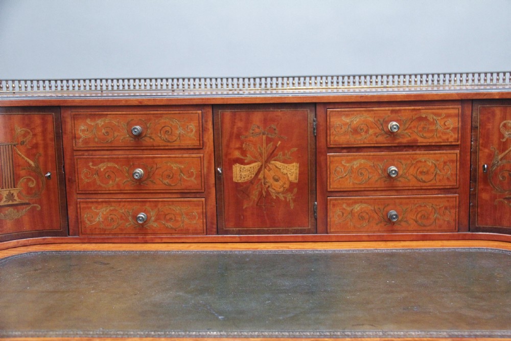 A 19th-century satinwood Carlton House writing desk featuring decorative marquetry, small drawers on a U-shaped superstructure, and tapered square legs with brass castors. View XIII
