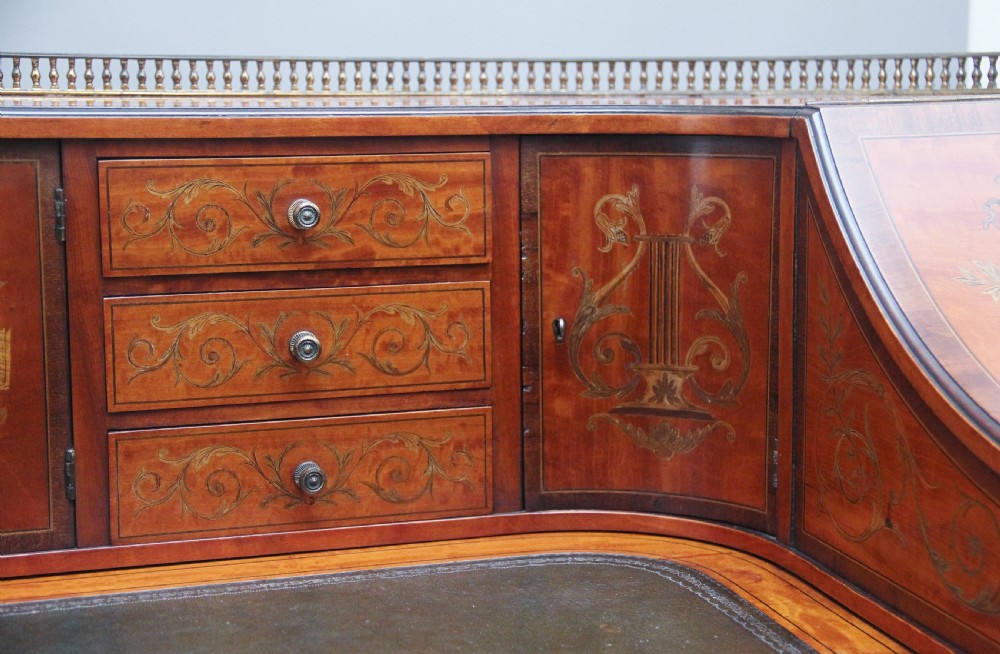 A 19th-century satinwood Carlton House writing desk featuring decorative marquetry, small drawers on a U-shaped superstructure, and tapered square legs with brass castors. View XIV