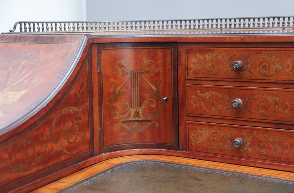A 19th-century satinwood Carlton House writing desk featuring decorative marquetry, small drawers on a U-shaped superstructure, and tapered square legs with brass castors. View XV
