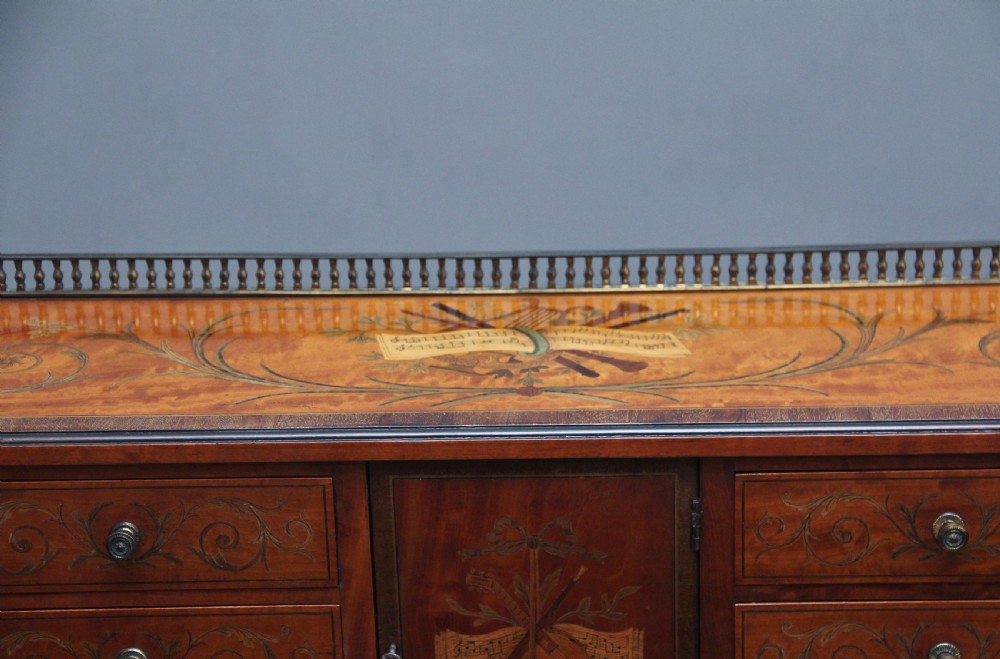 A 19th-century satinwood Carlton House writing desk featuring decorative marquetry, small drawers on a U-shaped superstructure, and tapered square legs with brass castors. View XVIII