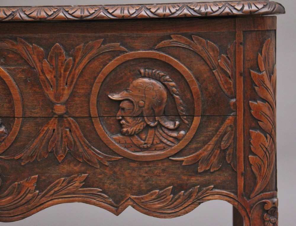 An early 19th-century French carved oak coffer featuring three carved profile medallions, acanthus leaf relief work, a scalloped apron, and cabriole legs. View IX
