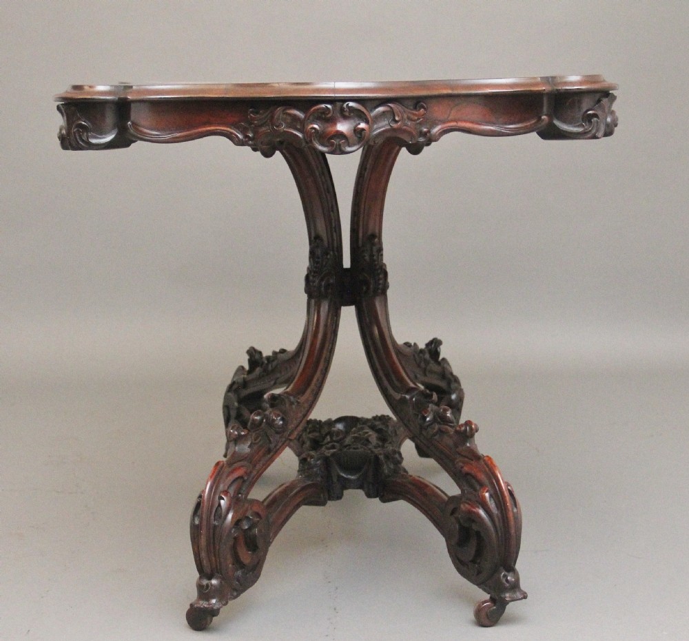 A 19th-century rosewood centre table featuring a serpentine top and carved C-scroll legs joined by a decorative stretcher. View VI