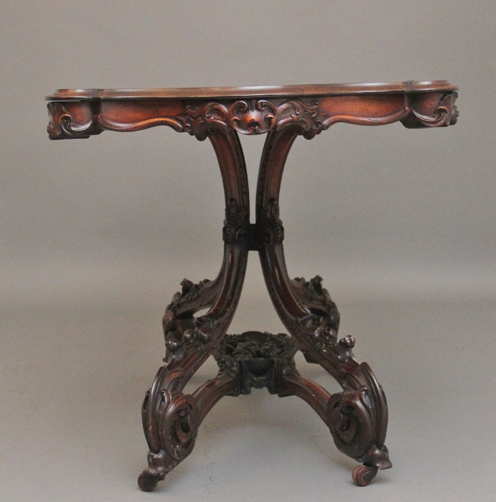 A 19th-century rosewood centre table featuring a serpentine top and carved C-scroll legs joined by a decorative stretcher. View VII