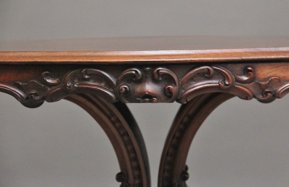 A 19th-century rosewood centre table featuring a serpentine top and carved C-scroll legs joined by a decorative stretcher. View X