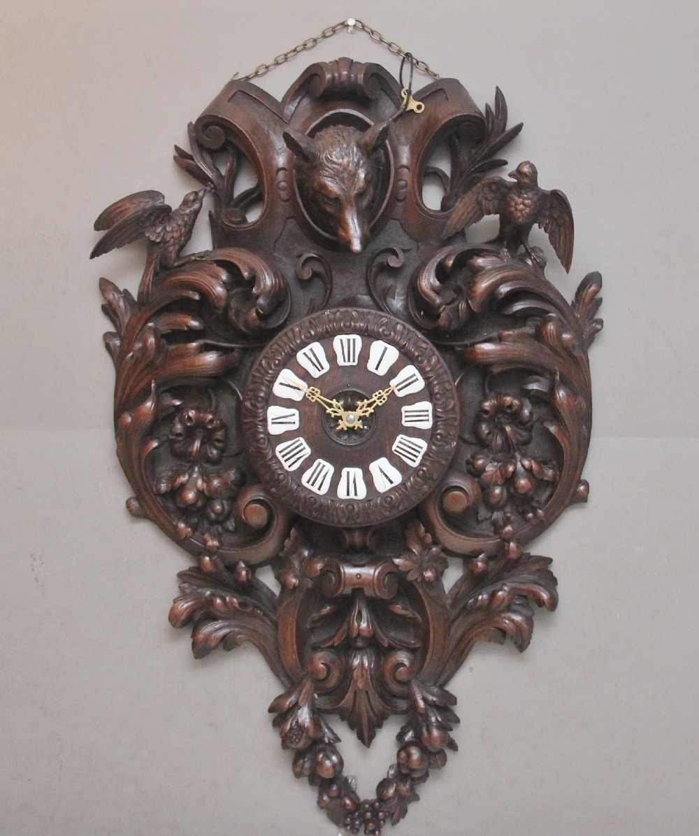 A 19th-century French carved dark oak wall clock featuring a central animal head carving, bird accents, leaf foliage, and white Roman numerals.