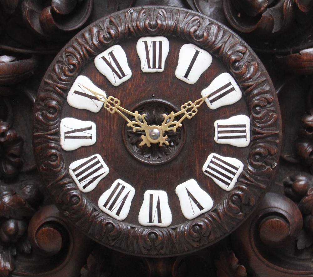 A 19th-century French carved dark oak wall clock featuring a central animal head carving, bird accents, leaf foliage, and white Roman numerals. View II