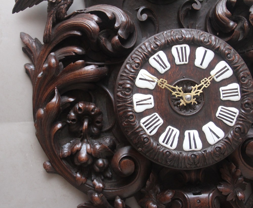 A 19th-century French carved dark oak wall clock featuring a central animal head carving, bird accents, leaf foliage, and white Roman numerals. View III