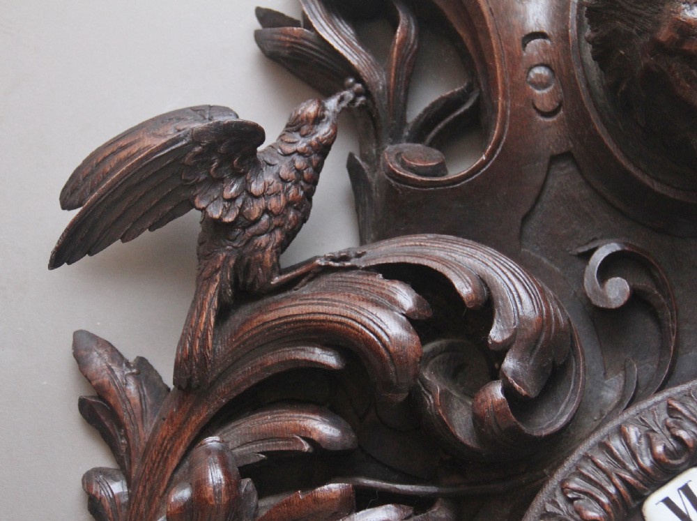 A 19th-century French carved dark oak wall clock featuring a central animal head carving, bird accents, leaf foliage, and white Roman numerals. View IV