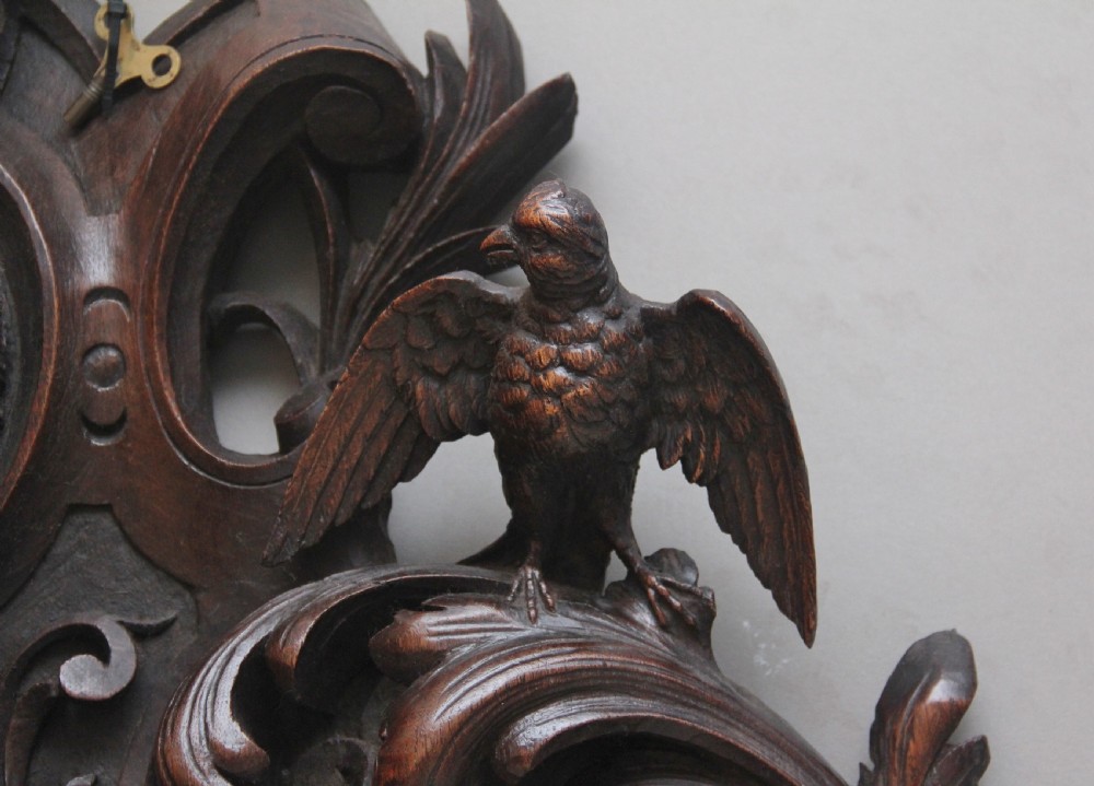 A 19th-century French carved dark oak wall clock featuring a central animal head carving, bird accents, leaf foliage, and white Roman numerals. View V