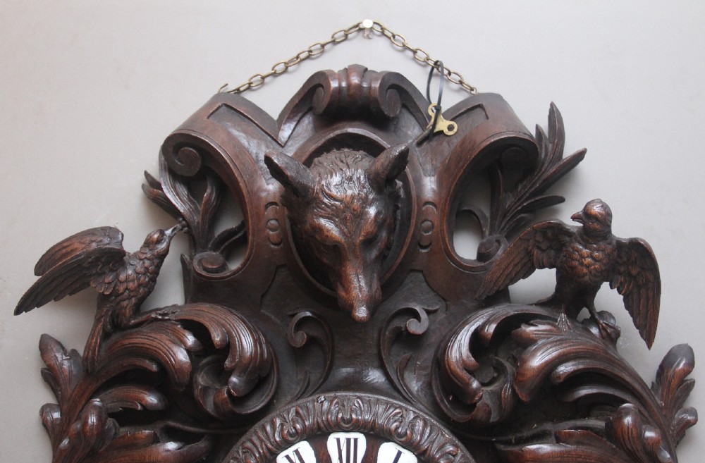 A 19th-century French carved dark oak wall clock featuring a central animal head carving, bird accents, leaf foliage, and white Roman numerals. View VI