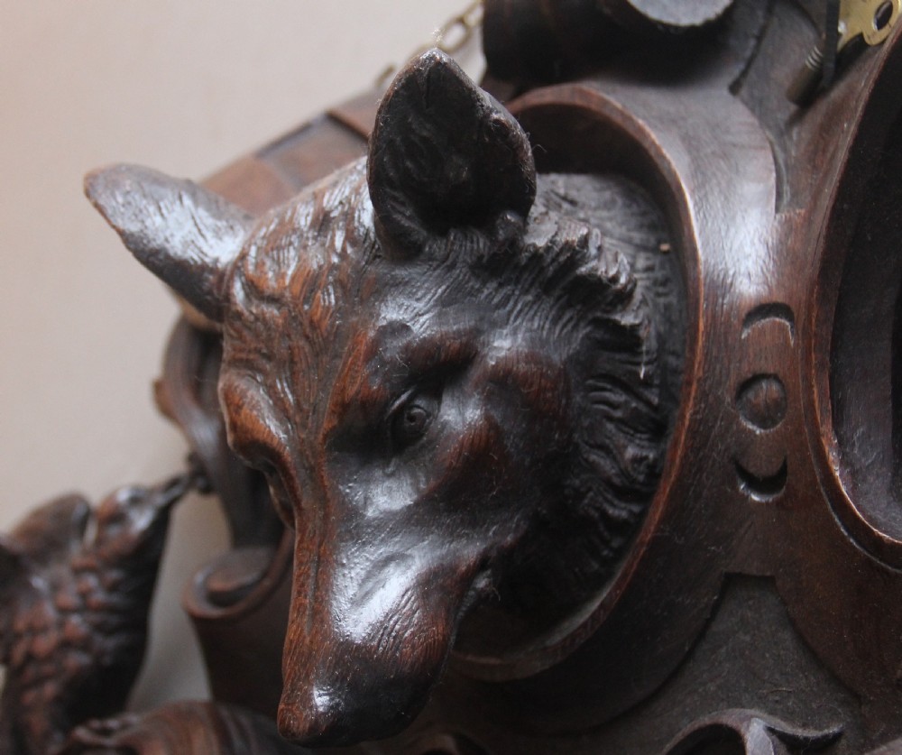 A 19th-century French carved dark oak wall clock featuring a central animal head carving, bird accents, leaf foliage, and white Roman numerals. View VII