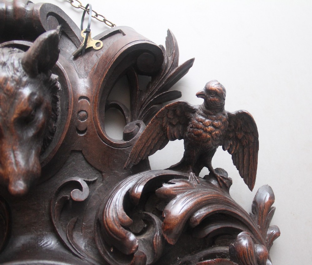A 19th-century French carved dark oak wall clock featuring a central animal head carving, bird accents, leaf foliage, and white Roman numerals. View VIII