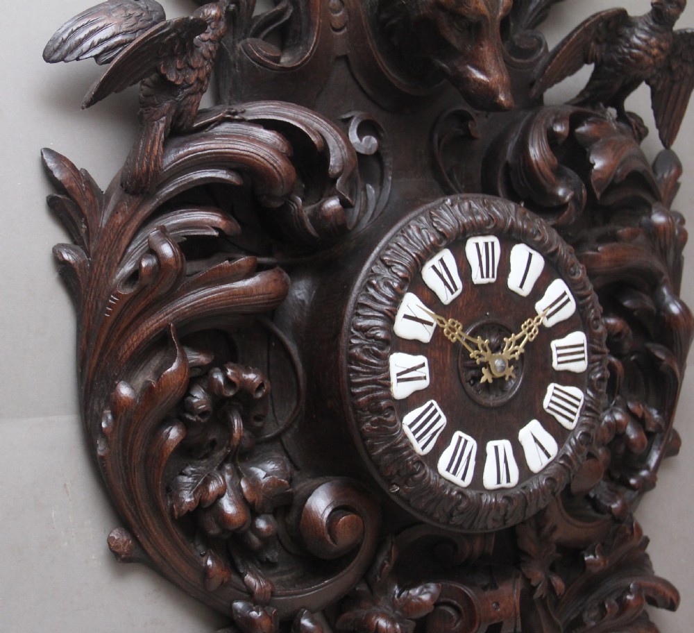 A 19th-century French carved dark oak wall clock featuring a central animal head carving, bird accents, leaf foliage, and white Roman numerals. View IX