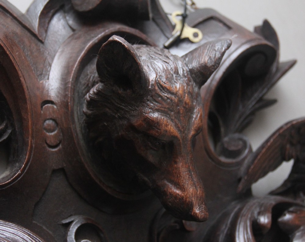 A 19th-century French carved dark oak wall clock featuring a central animal head carving, bird accents, leaf foliage, and white Roman numerals. View X