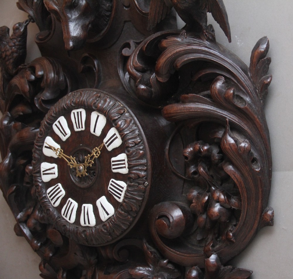 A 19th-century French carved dark oak wall clock featuring a central animal head carving, bird accents, leaf foliage, and white Roman numerals. View XI