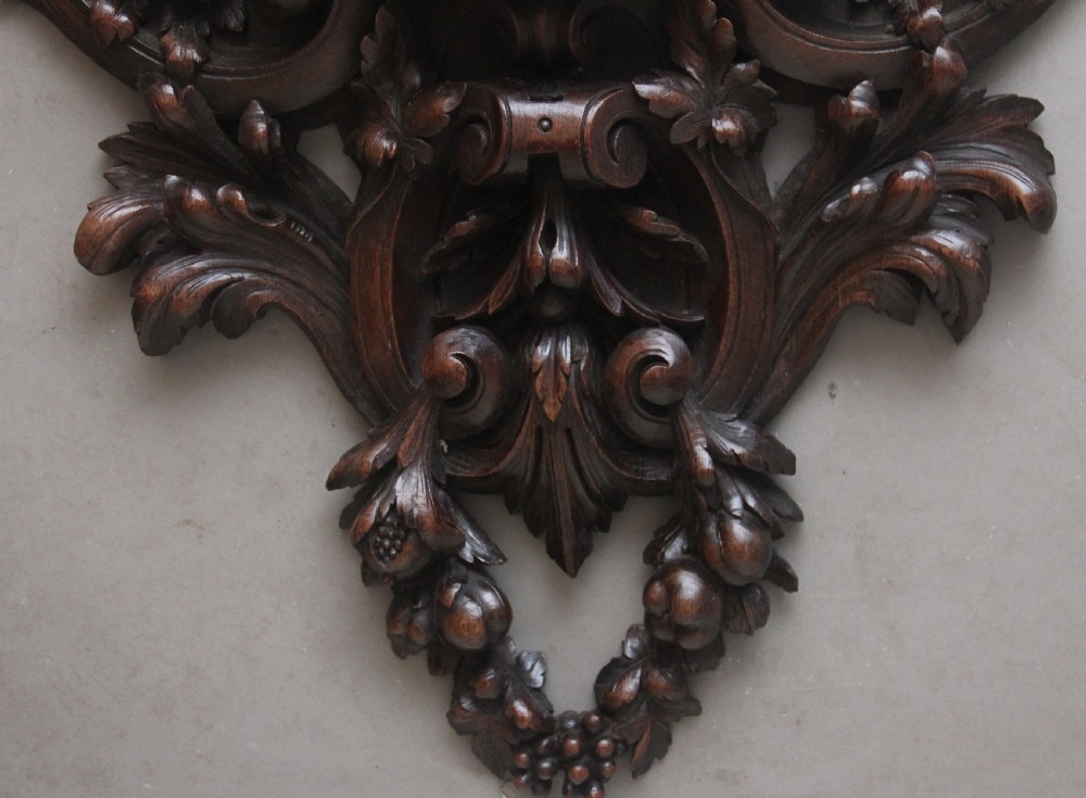 A 19th-century French carved dark oak wall clock featuring a central animal head carving, bird accents, leaf foliage, and white Roman numerals. View XII