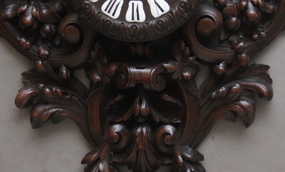 A 19th-century French carved dark oak wall clock featuring a central animal head carving, bird accents, leaf foliage, and white Roman numerals. View XIII