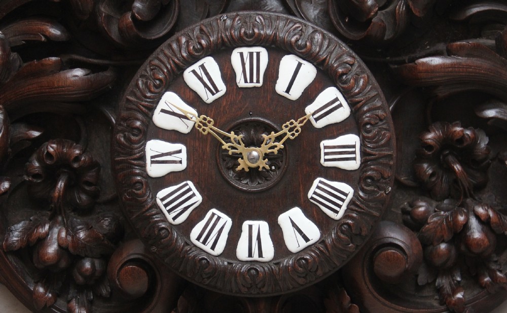 A 19th-century French carved dark oak wall clock featuring a central animal head carving, bird accents, leaf foliage, and white Roman numerals. View XIV