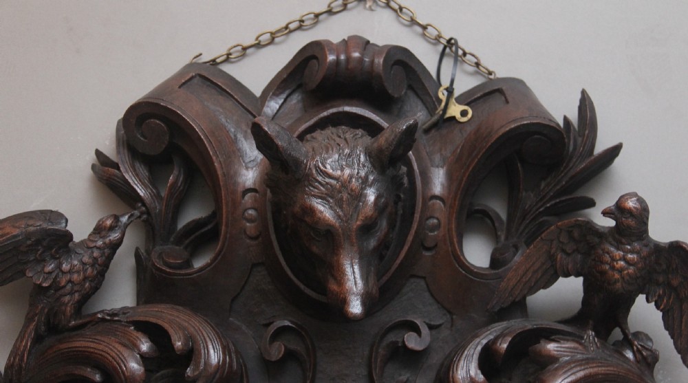 A 19th-century French carved dark oak wall clock featuring a central animal head carving, bird accents, leaf foliage, and white Roman numerals. View XV