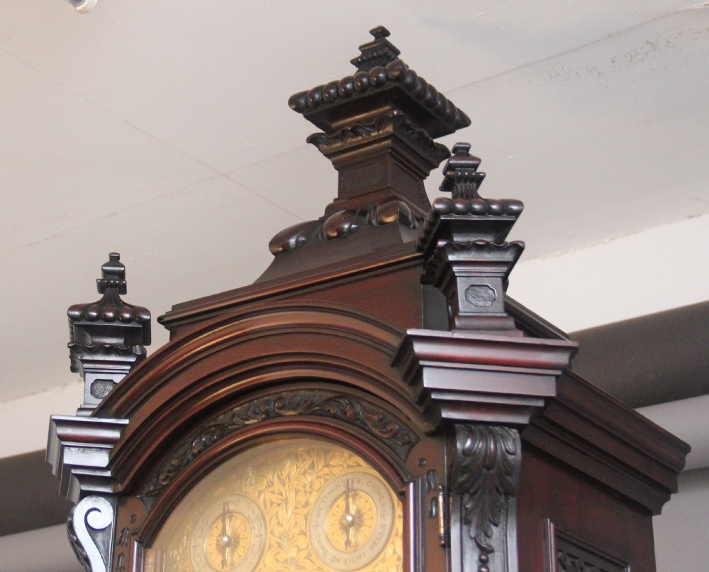 An early 20th-century carved dark mahogany longcase clock featuring an ornate pediment, carved trunk door, and etched brass dial. View V