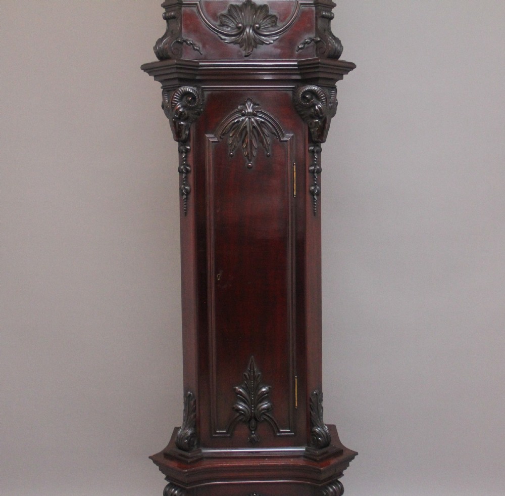 An early 20th-century carved dark mahogany longcase clock featuring an ornate pediment, carved trunk door, and etched brass dial. View XI