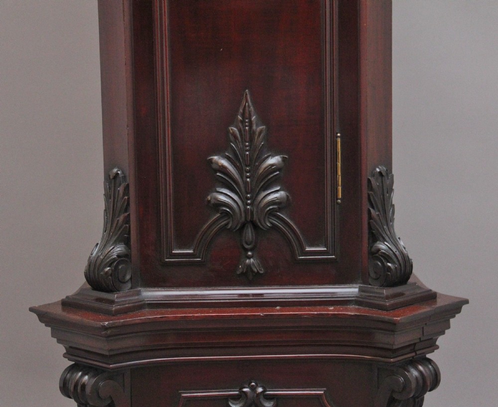 An early 20th-century carved dark mahogany longcase clock featuring an ornate pediment, carved trunk door, and etched brass dial. View XIII