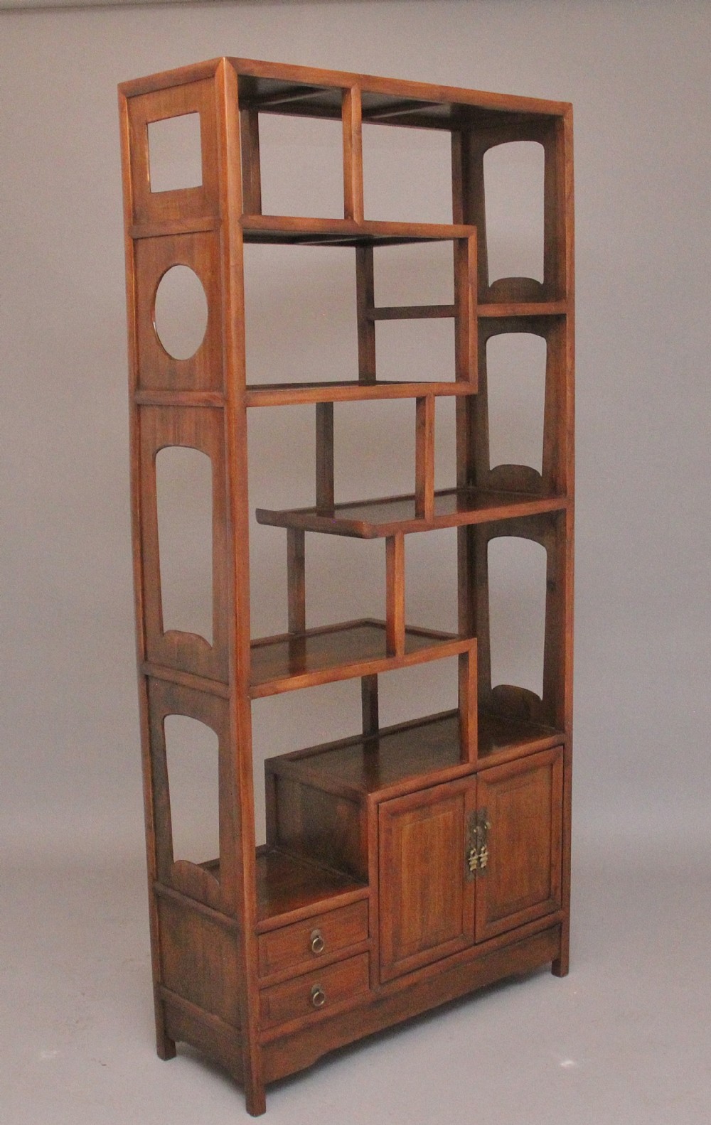 An early 20th-century Chinese hardwood duobaoge cabinet featuring asymmetrical open shelving, geometric side cut-outs, and lower drawers with brass hardware.